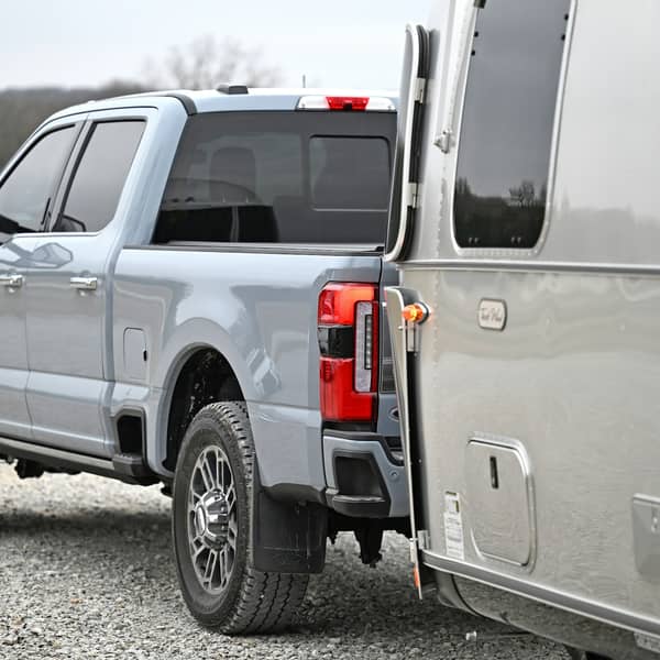Light gray pickup hitched to a silver travel trailer on gravel