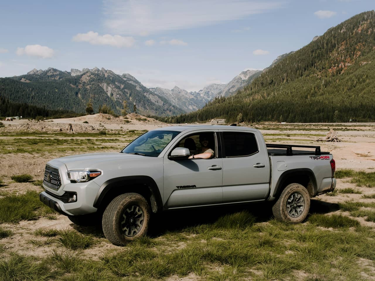 Gray Toyota Tacoma parked on a grassy valley floor below mountains
