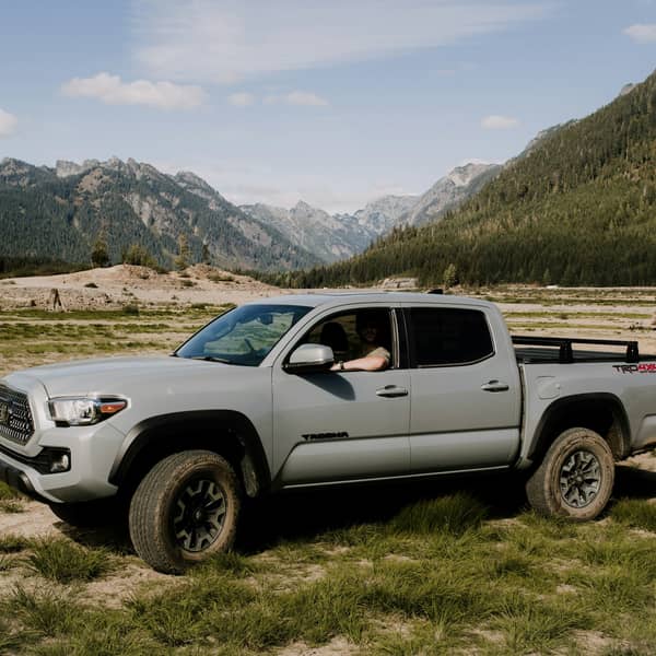 Gray Toyota Tacoma parked on a grassy valley floor below mountains